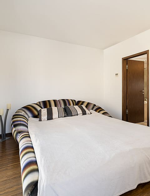 Modern bedroom featuring dark hardwood floors and a French balcony overlooking the historic rooftops of Palma.