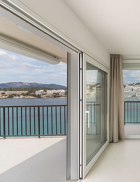 An interior view of large sliding glass doors opening onto a balcony with a black railing, overlooking a bay and hills.