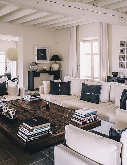Spacious living room featuring white sofas, a dark wood coffee table, and exposed white-painted wooden ceiling beams.