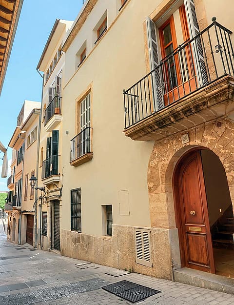Exterior view of a multi-story townhouse in a narrow cobblestone street, featuring a stone arched entrance and iron balcony.