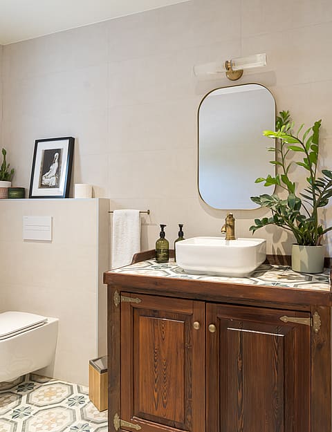 A bathroom featuring a dark wood vanity cabinet, white vessel sink, patterned floor tiles, and a wall-mounted toilet.