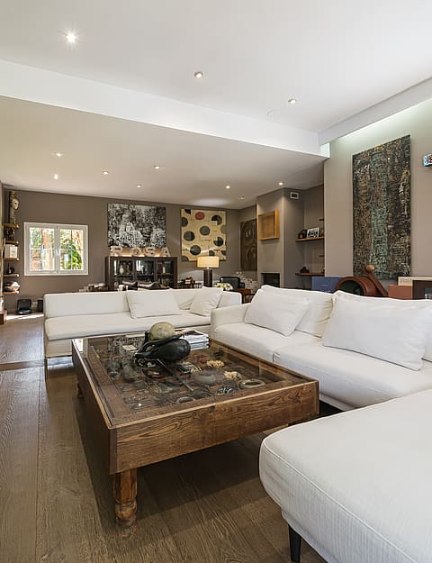 Spacious living room featuring white modular sofas, a stone-topped coffee table, and beige tiled floors under recessed lighting.