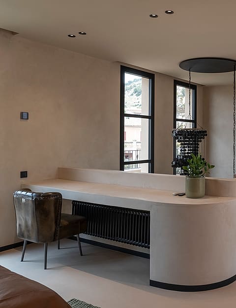A minimalist home office area with a curved plaster desk and a stone staircase in a neutral, modern townhouse interior.
