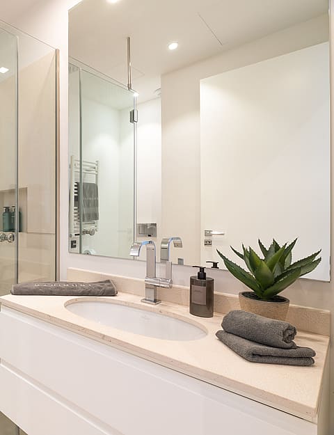 Modern bathroom featuring a white vanity with cream stone top, glass-enclosed walk-in shower, and heated towel rail.