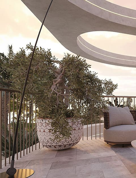 A modern curved terrace overlooking the sea at sunset, featuring stone flooring, outdoor seating, and a large potted plant.