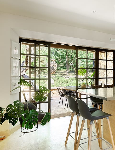 Modern kitchen with light wood cabinetry, stone-topped island, and black metal framed glass doors opening to a garden patio.