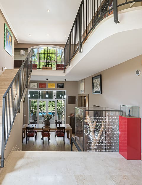 An expansive entrance hall with a polished stone staircase and ornate metal railings, looking towards a dining area beyond.