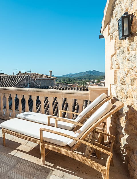 Outdoor seating and sun loungers on a rooftop terrace overlooking village rooftops and hills