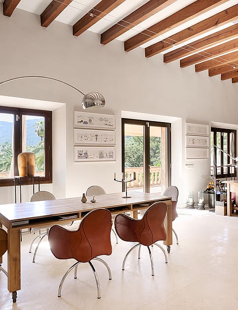 Spacious living room with exposed wood ceiling beams, white plaster walls, dining table with leather chairs, and fireplace.