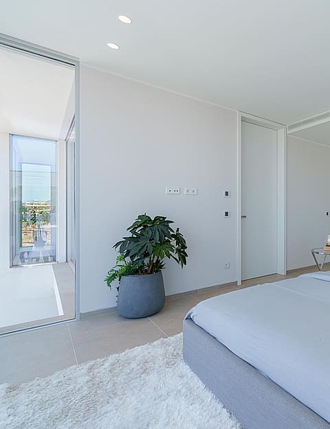 A modern bedroom with a grey upholstered bed, mirrored wall panels, and a shaggy white rug on a tiled floor.