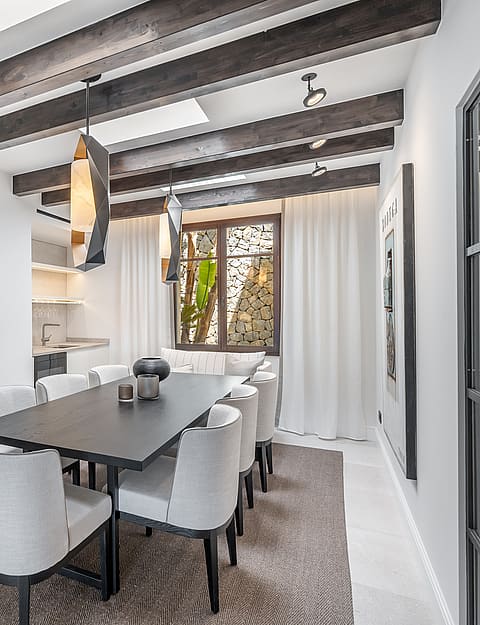 Modern dining room featuring a dark wood table, grey upholstered chairs, exposed ceiling beams, and integrated skylights.