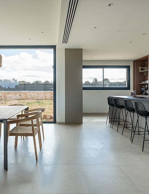 A modern, open-plan dining and kitchen area with polished concrete floors, wooden furniture, and mountain views through windows.