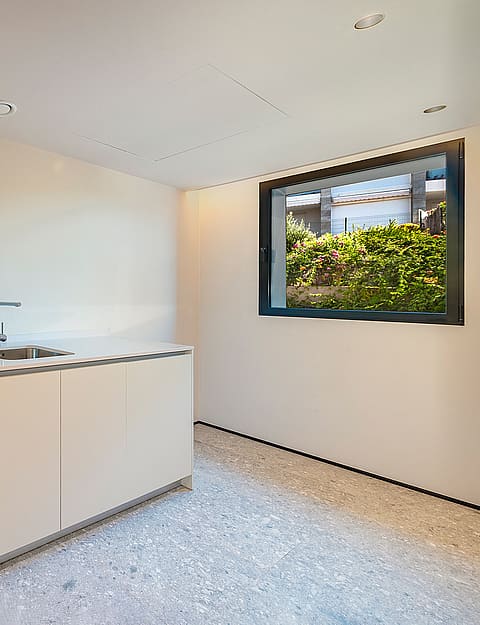 A minimalist laundry room featuring white front-loading appliances, a built-in sink, and speckled stone flooring.
