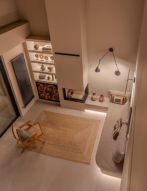 High-angle view of a minimalist seating area featuring a corner fireplace, low-profile bench, and illuminated display shelves.