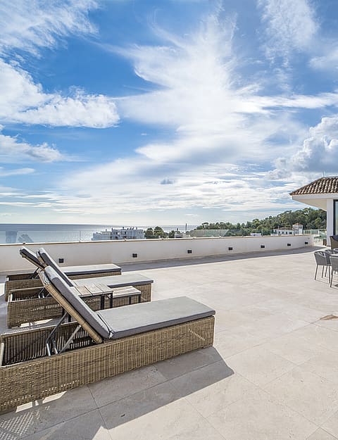 A wide outdoor terrace in Illetas featuring sun loungers, an outdoor dining table, and direct views of the Mediterranean sea.