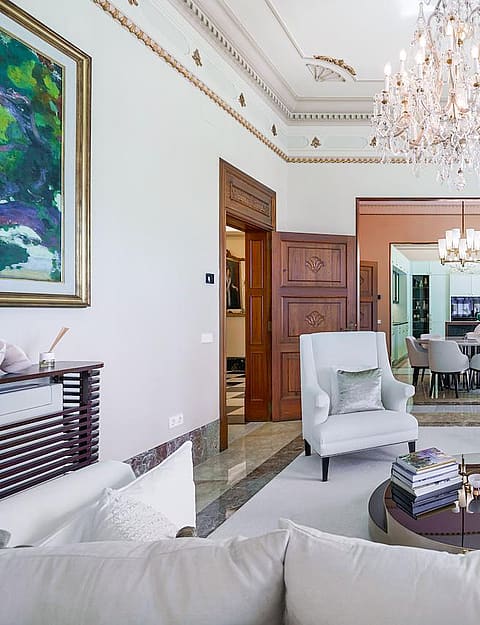 A formal living room with cream walls, detailed crown molding, a crystal chandelier, and view through to the dining area.