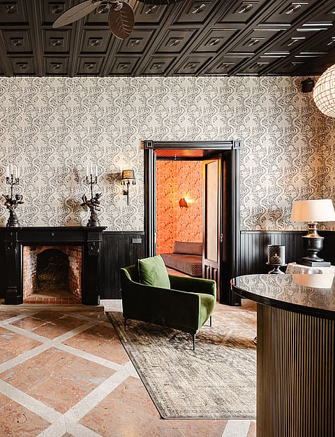 A formal living area featuring intricate patterned wallpaper, a black coffered ceiling, and a central stone fireplace.