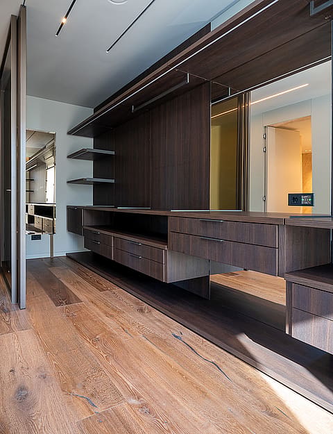 A modern walk-in closet with dark wood storage units, integrated LED lighting, and light-toned oak hardwood flooring.