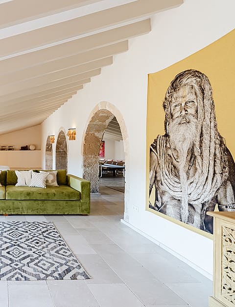 Wide shot of a bright attic living space featuring a long olive green velvet sofa, white tiled floor, and exposed timber beams.