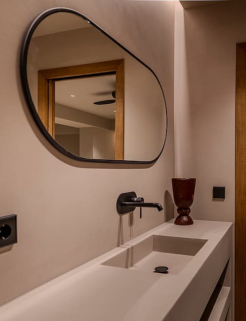 A contemporary bathroom detail featuring an integrated stone sink, a matte black wall-mounted faucet, and an oval mirror.