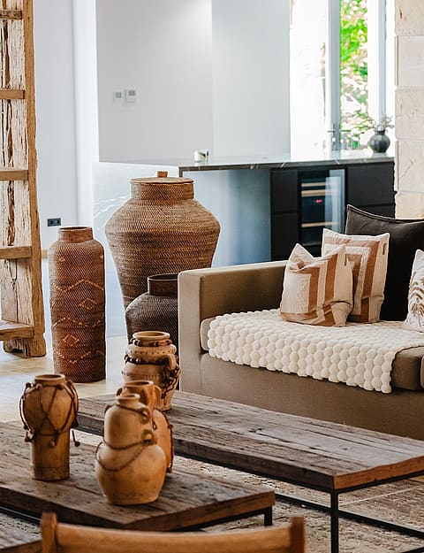 Interior view of a living room featuring a textured stone wall, a neutral sofa with decorative cushions, and rustic wooden decor items.