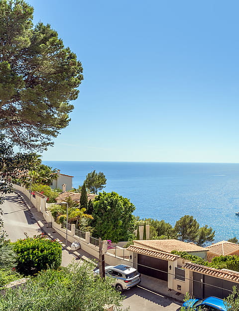 Elevated perspective of a coastal residential street overlooking the blue Mediterranean sea with several small boats.