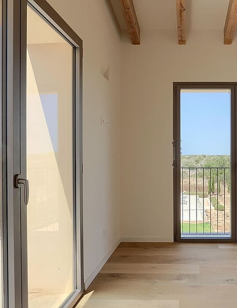 Unfurnished bedroom with wooden beamed ceiling, oak flooring, and glass doors opening to a private balcony with mountain views.