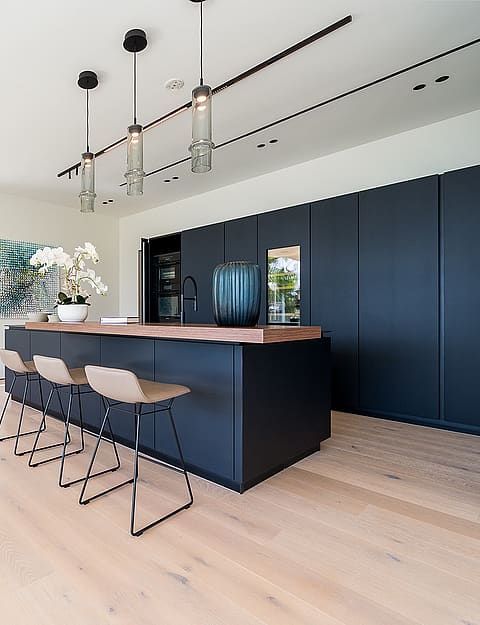 Modern open-plan kitchen featuring a dark matte island, light oak hardwood floors, and three pendant lights in Son Vida.