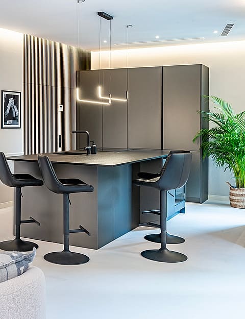 A modern open-plan interior featuring a dark kitchen island with bar stools, neutral textured seating, and wall moldings.