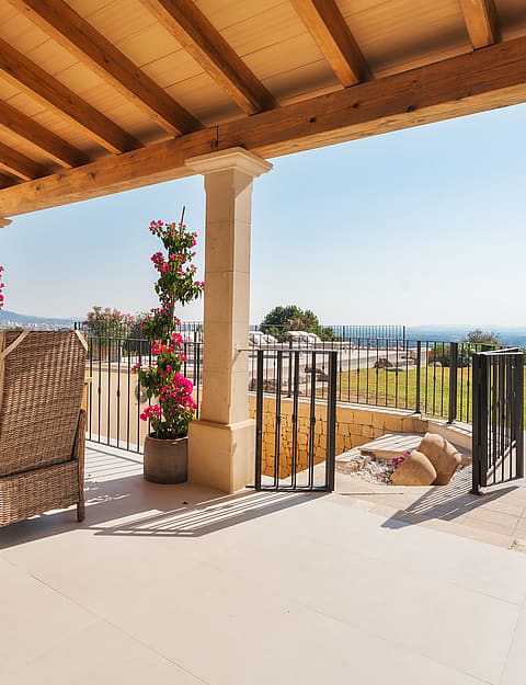 Comedor exterior en terraza con muebles de mimbre, vigas de madera y vistas al paisaje de montaña.