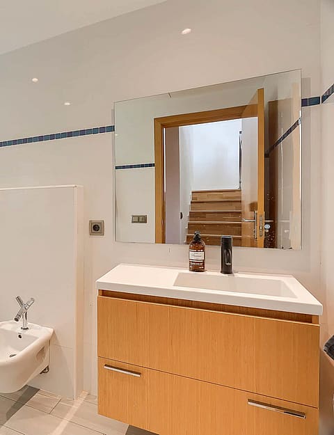 Bright bathroom featuring a walk-in shower with glass partition, wall-hung toilet, bidet, and a wooden vanity unit with mirror.