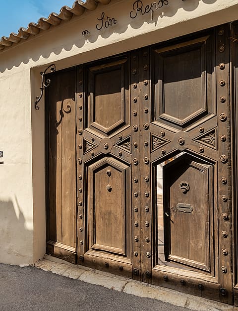 Heavy dark wood gate with iron studs and an inset pedestrian door set into a stone wall under tiled eaves.