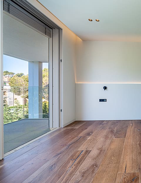 Empty bedroom with light-colored walls, recessed strip lighting, and wide-plank wood flooring opening to a terrace.
