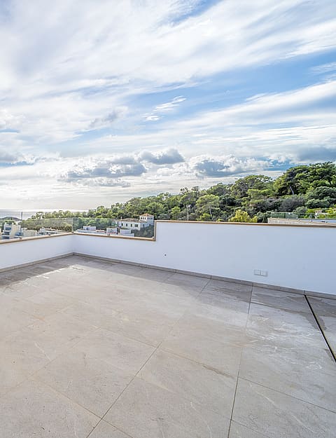 Empty rooftop terrace with white parapet walls, glass balustrade, and wide Mediterranean sea view in Illetas.