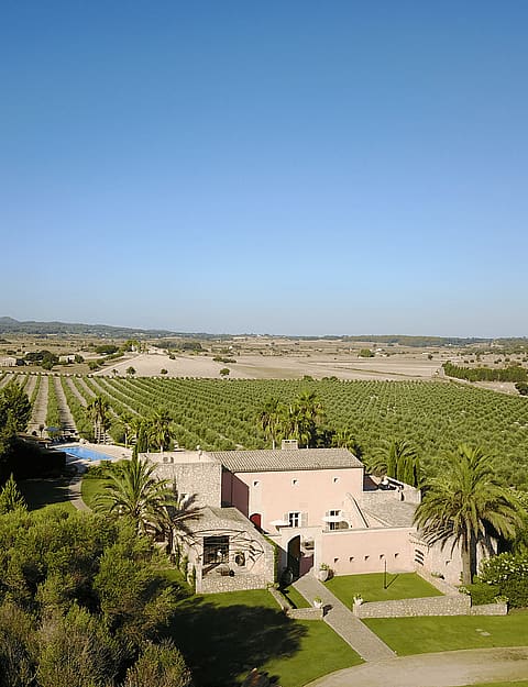 Aerial drone shot of a pink-walled Finca surrounded by vast agricultural fields and Mediterranean landscape.