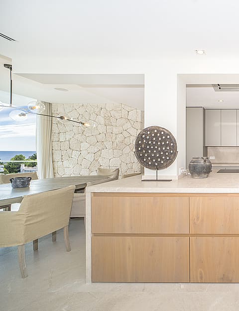 Modern open-plan kitchen featuring a large wooden island with a stone countertop and light wood cabinets, set against a white wall.