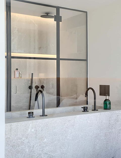 Close up of a bathroom vanity with terrazzo countertop, black metal-framed glass shower partition, and vertical wood wall paneling.