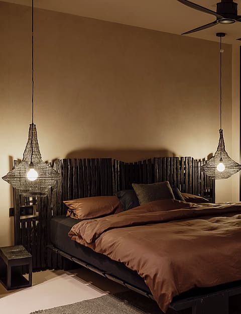 Bedroom with a queen-sized bed, dark wood headboard, and two decorative pendant lights. Large sliding glass door reveals a night view of hills.