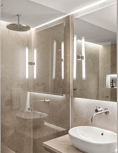 Modern bathroom featuring marble walls, a glass walk-in shower with rainfall head, and mirrors with integrated lighting.
