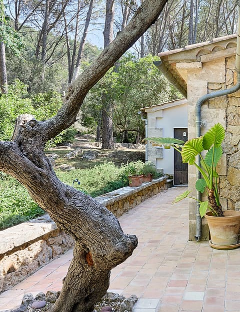 A covered stone terrace featuring a wooden dining table and chairs, set against a rustic fieldstone wall.