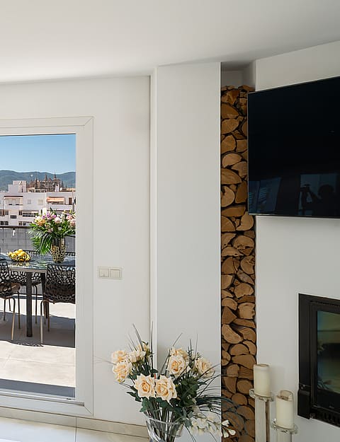 Living room with beige sofa, integrated fireplace with stacked firewood, and sliding glass doors opening to a city terrace.