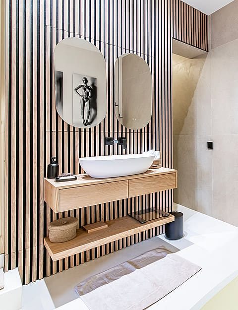 Bathroom interior featuring a white vessel sink on a wooden floating vanity, oval mirrors, and a decorative ladder towel rack.