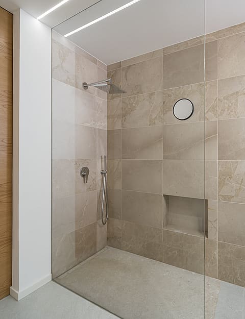 A walk-in shower with large-format beige stone tiles, a glass partition, and integrated recessed shelving.