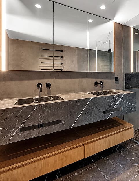 Modern bathroom featuring a floating grey marble double vanity with matte black fixtures, integrated LED mirror lighting, and a glass-enclosed rain shower.