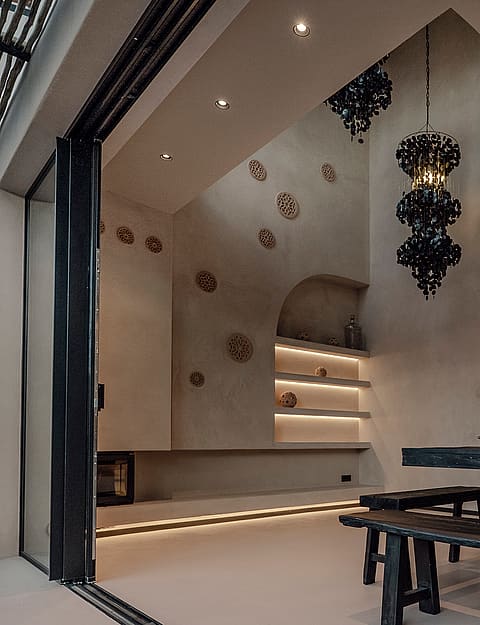Dining area featuring a dark wooden farmhouse table and benches, sculptural black pendant lights, and arched wall niches with soft integrated illumination.