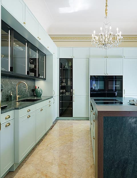 Modern kitchen with light green cabinetry, a dark marble kitchen island, a crystal chandelier, and balcony doors.
