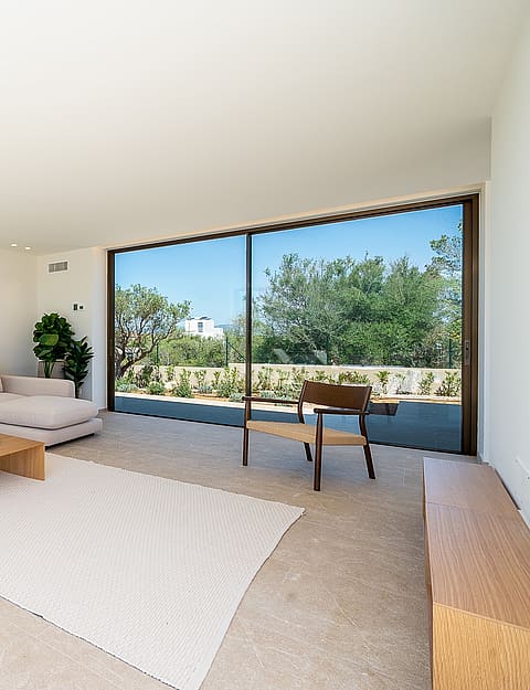Modern living room featuring a beige sectional sofa, low wooden coffee table, and large sliding glass doors opening to a garden.
