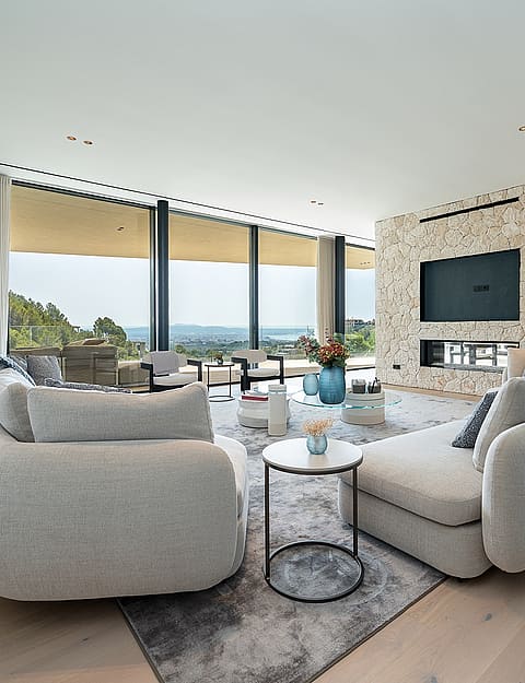 Contemporary living room with light oak floors, a textured stone fireplace wall, and floor-to-ceiling windows facing the sea.