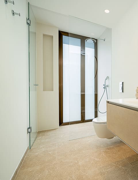 Bright bathroom with a floating beige vanity, white countertop, irregular shaped mirror, and glass-enclosed shower area.