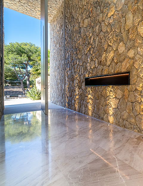 Interior entrance hall featuring a large natural stone wall with an integrated horizontal fireplace, polished stone floors, and recessed lighting.